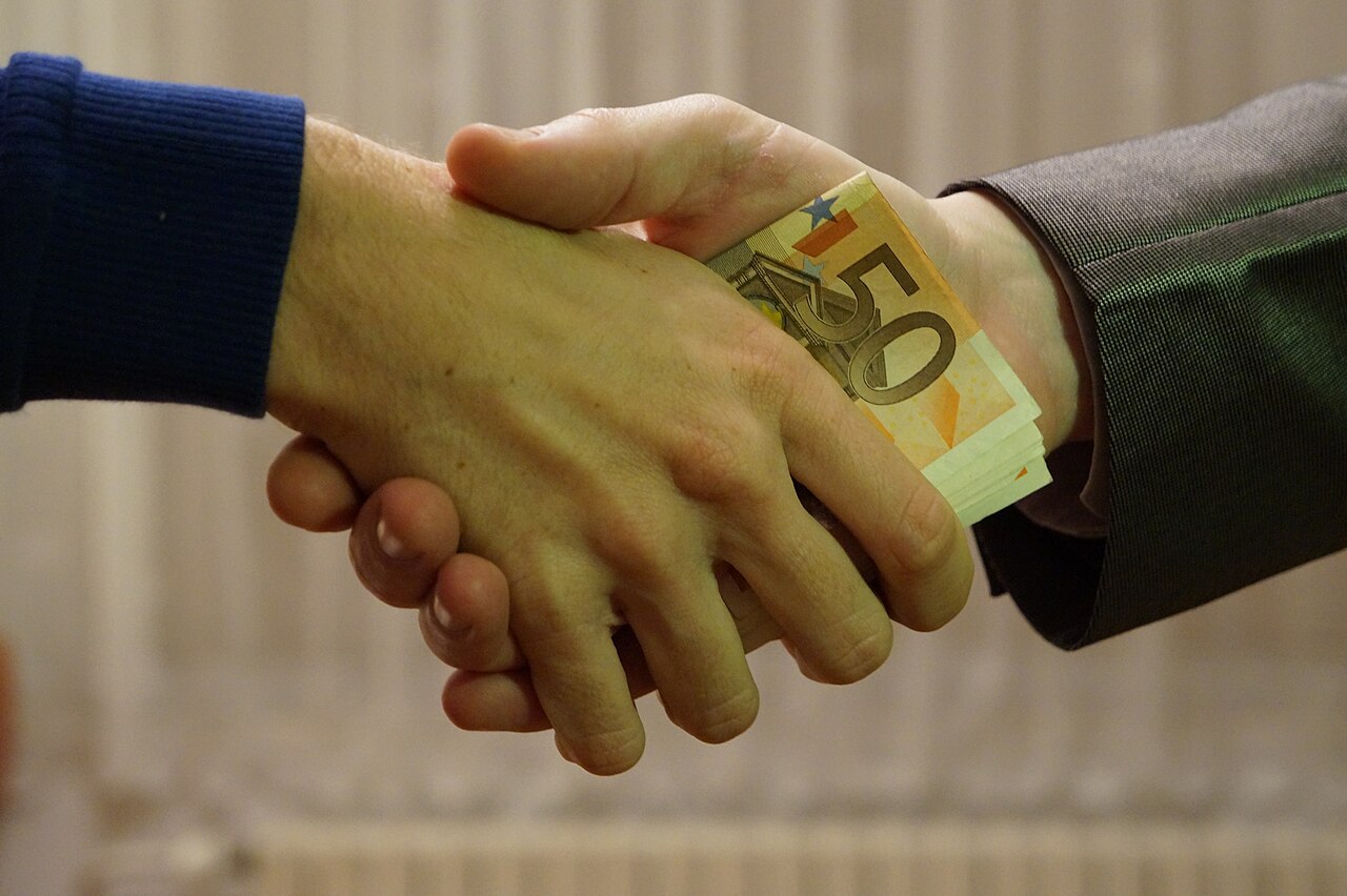 Dos manos se estrechan con billetes de euro